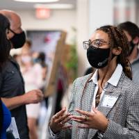Scholar wearing mask presenting poster to one guest.
